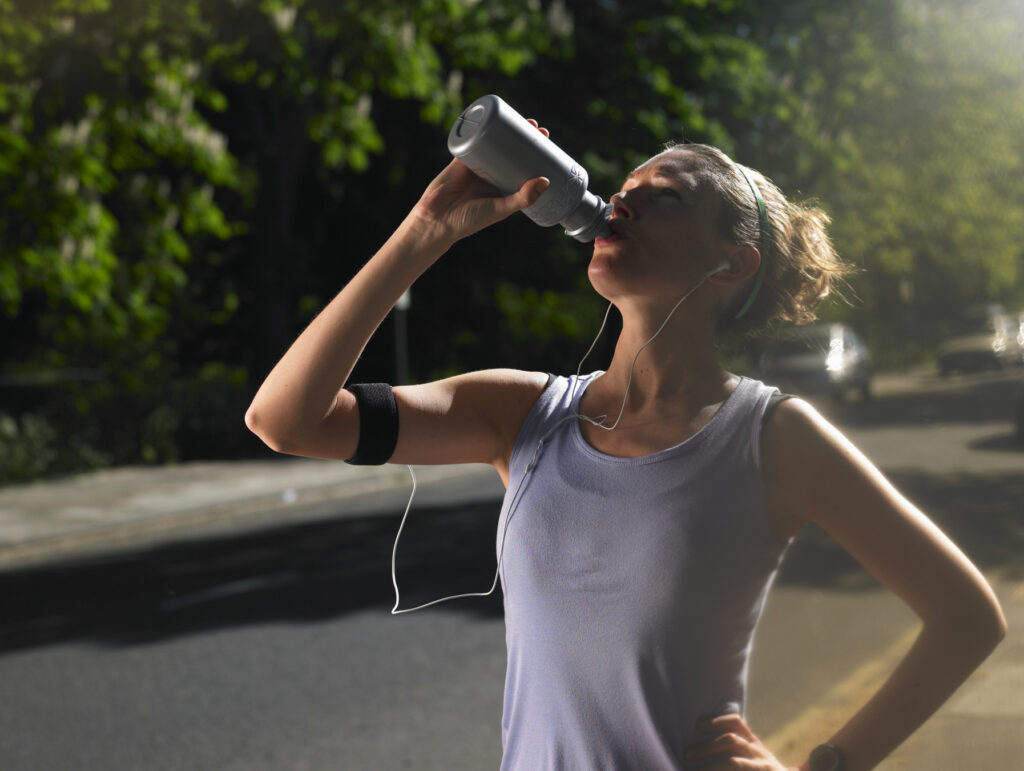 Young woman standing at street, drinking after jogging